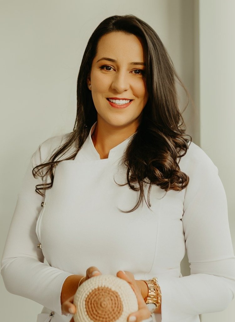 Julia Dill de jaleco segurando uma mama de crochê usada nas orientações de amamentação